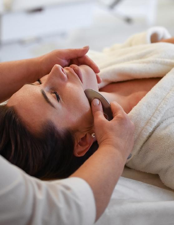 Relaxed woman receiving a Gua Sha sculpting facial, illustrating how this treatment improves facial contours, boosts circulation, and promotes a radiant, youthful appearance.